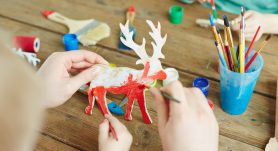 Hands of adult and kid painting wooden deer in red